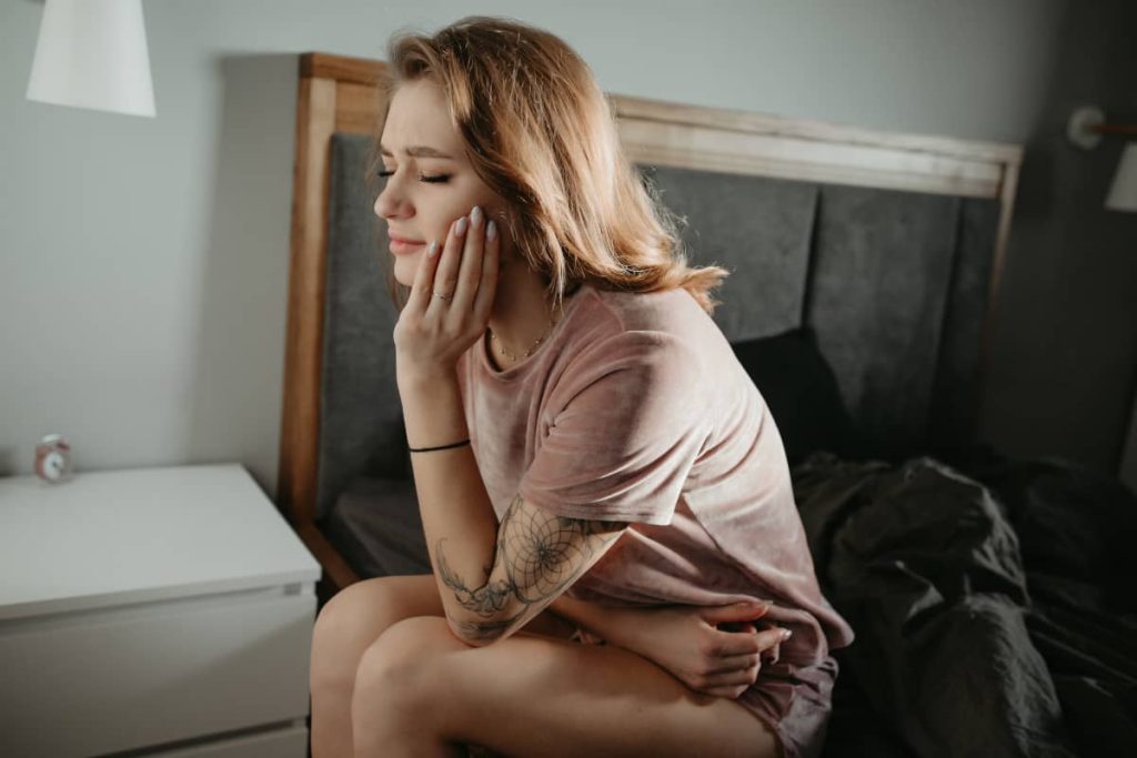 femeie tanara cu durere de masea sta pe marginea patului cu mana la obraz