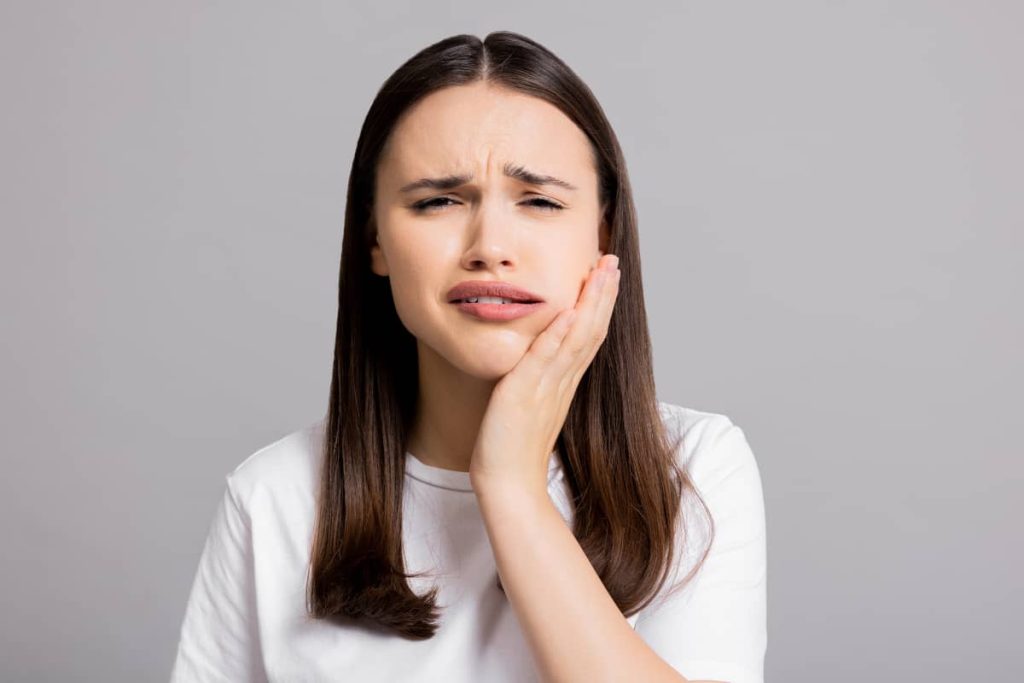 femeie tanara cu abces dentar tine mana pe obrazul umflat